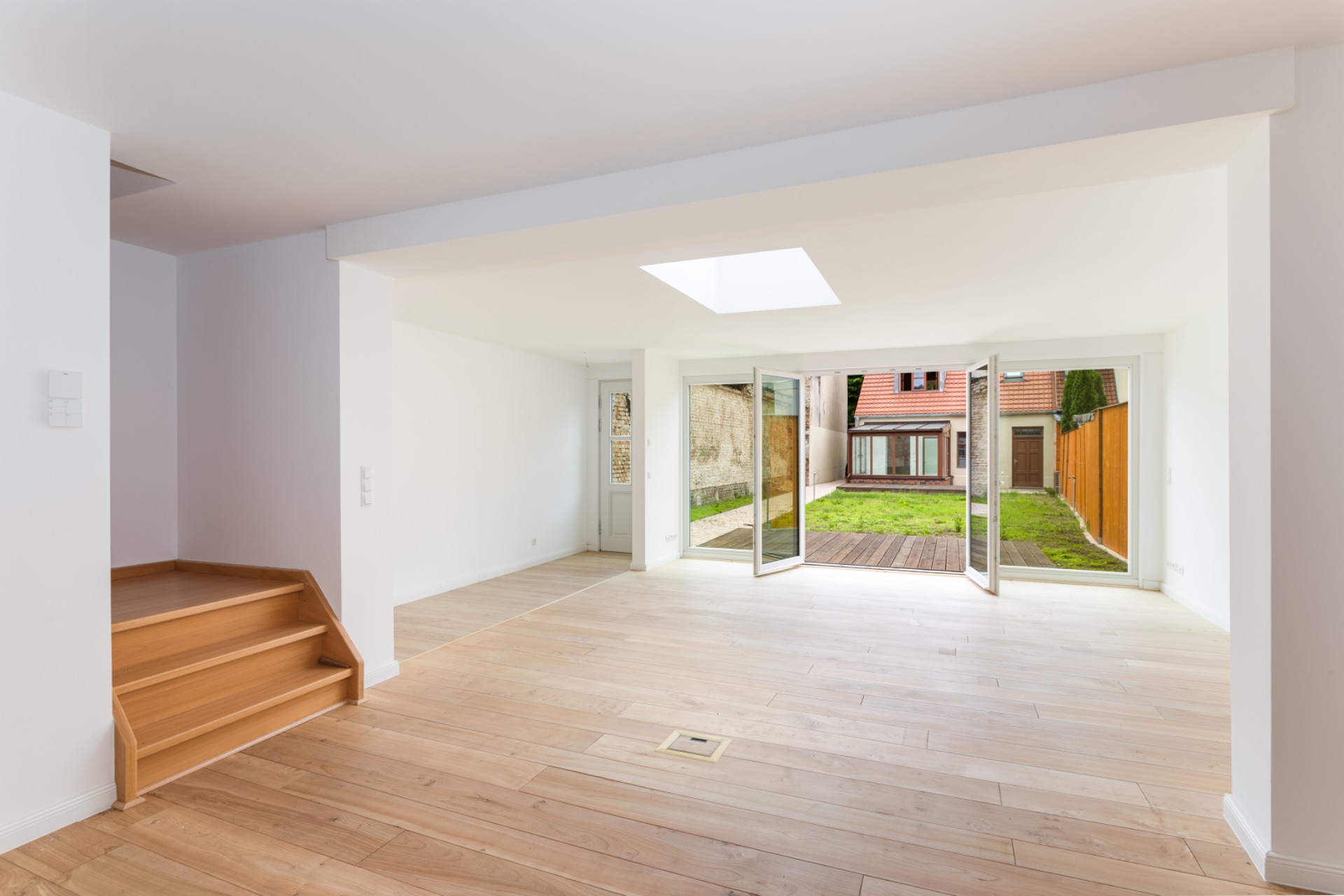 Helles Wohnzimmer mit Holzboden, Stufen und großen Fenstertüren zum Garten.