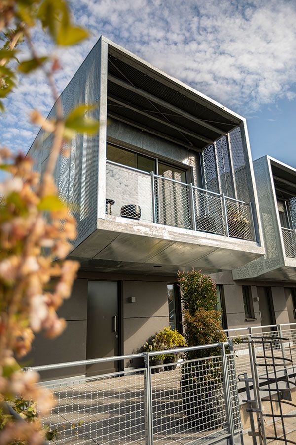 Moderne Wohnung mit Metallbalkon und großem Fenster, vorne Pflanzen und ein Zaun.