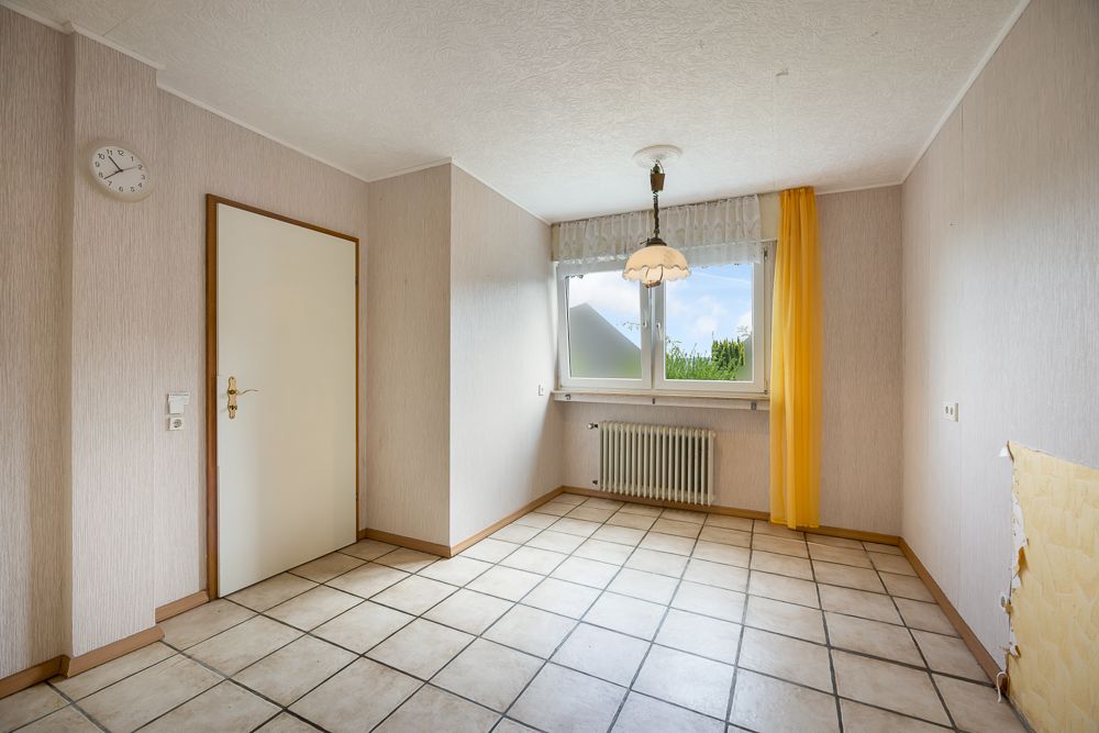 Leerer Raum mit Fliesenboden, Fenster, Heizung und gelbem Vorhang.