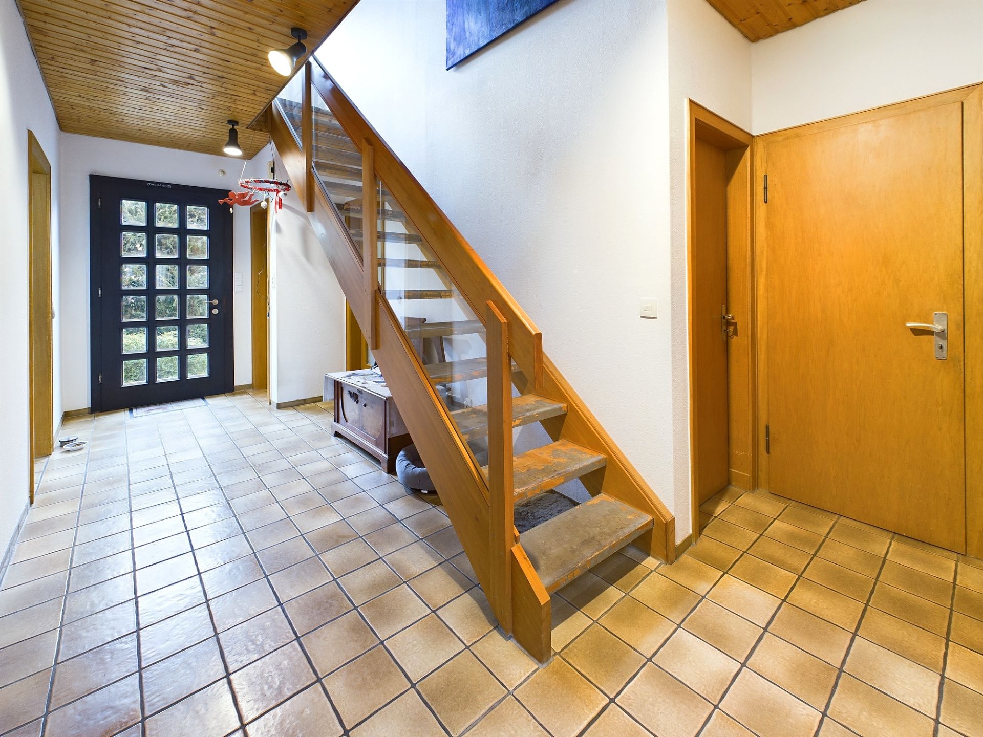 Flur mit Holztreppe, Fliesenboden und mehreren Holztüren in einem Wohnhaus.