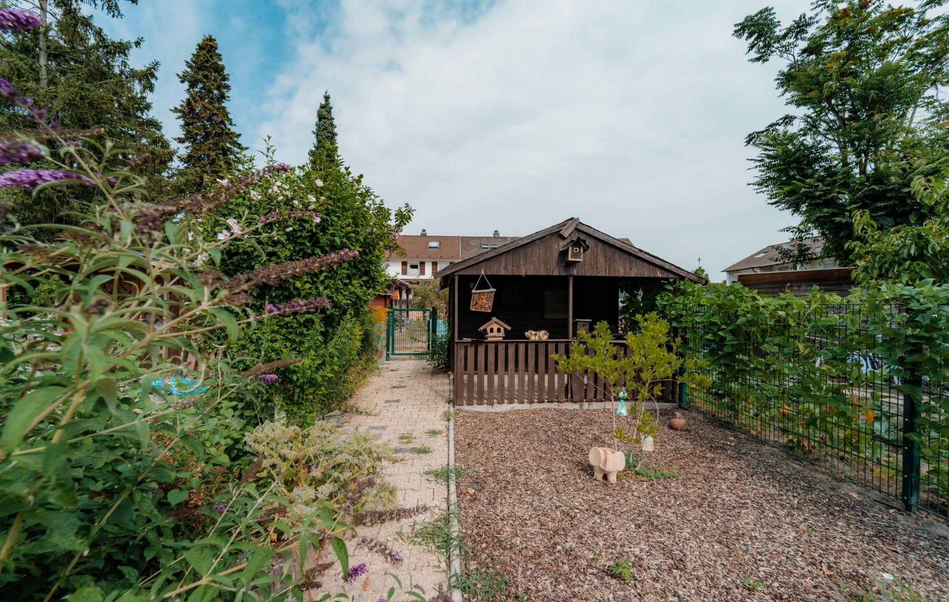 Garten mit einem Holzhaus, Gartenweg und vielen Pflanzen im Vordergrund.