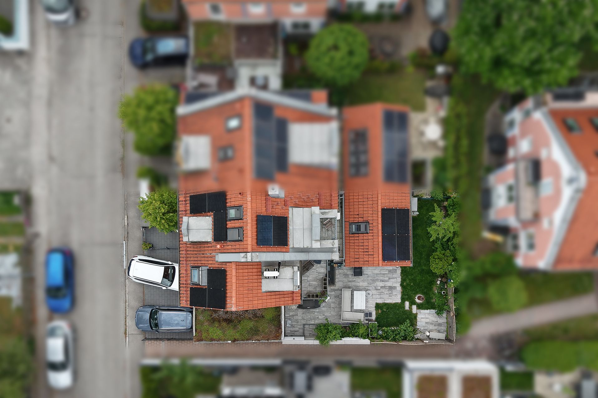 Luftaufnahme eines Hauses mit rotem Dach, Terrasse und umgebendem Garten.