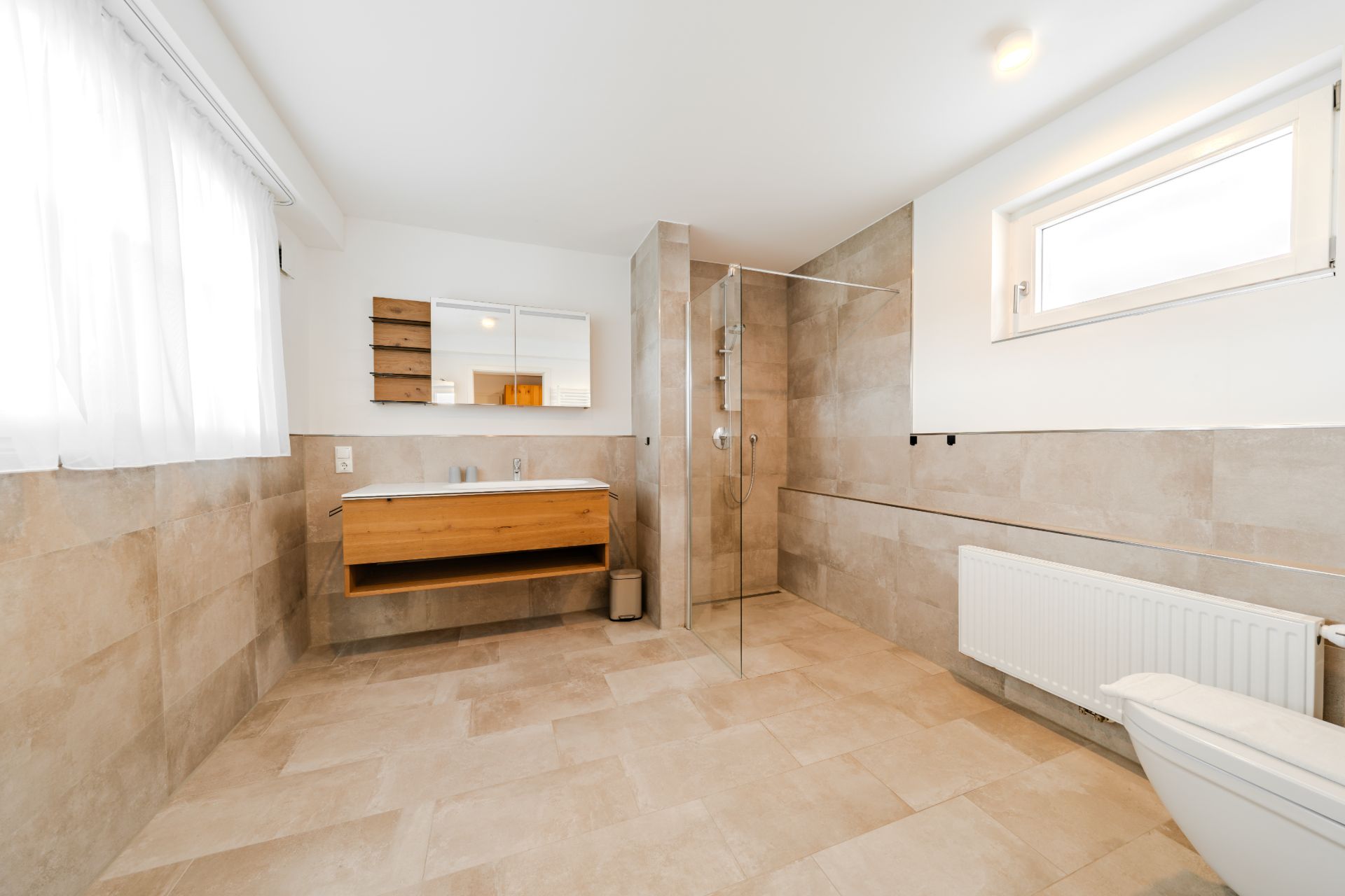 Modernes Badezimmer mit begehbarer Dusche, Waschbecken, Spiegel und Fenster.