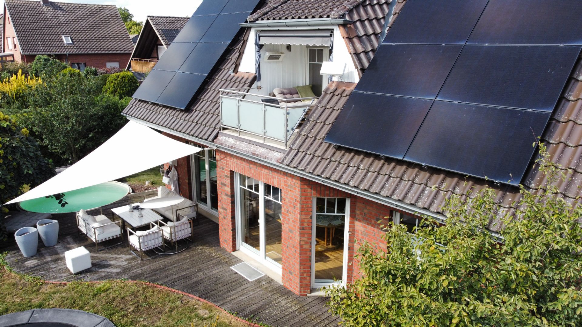 Backsteinwohnhaus mit Solarpanels, Balkon und Terrasse mit Gartenmöbeln.