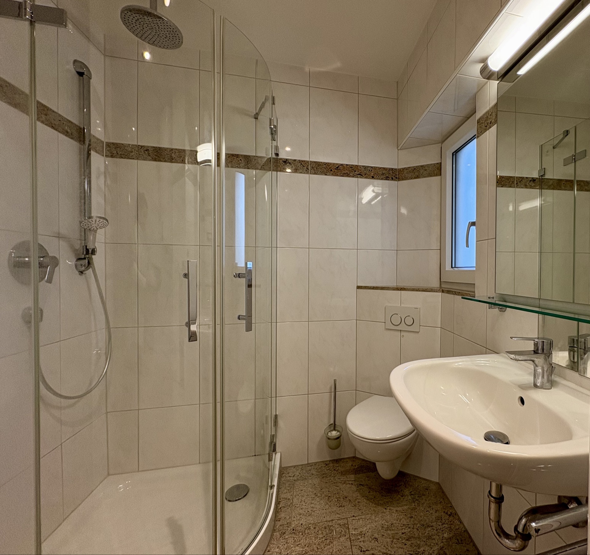 Modernes Badezimmer mit Dusche, WC, Waschbecken und Fenster.
