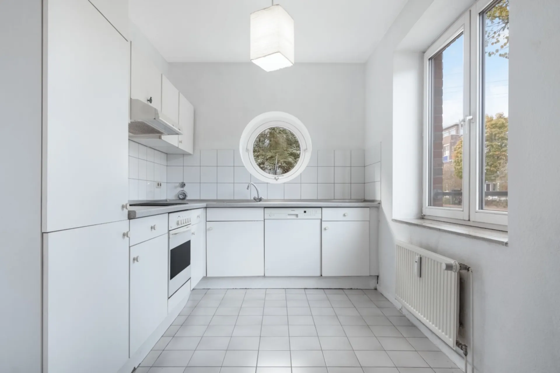 Helle, weiße Einbauküche mit rundem Fenster und großem rechteckigen Fenster.