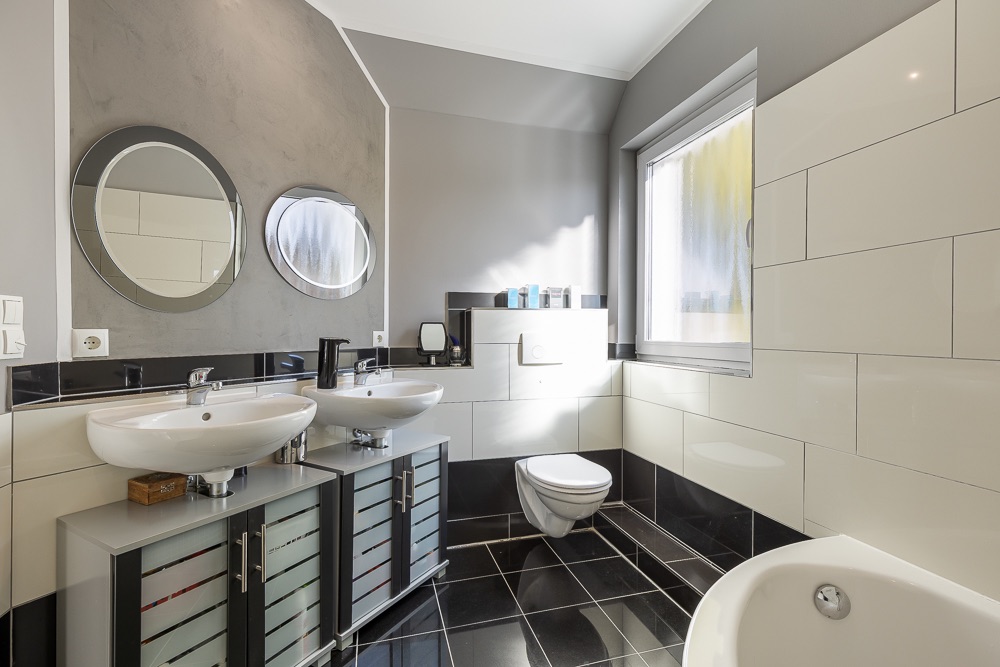 Modernes Badezimmer mit zwei Waschbecken, runden Spiegeln, WC und Badewanne.