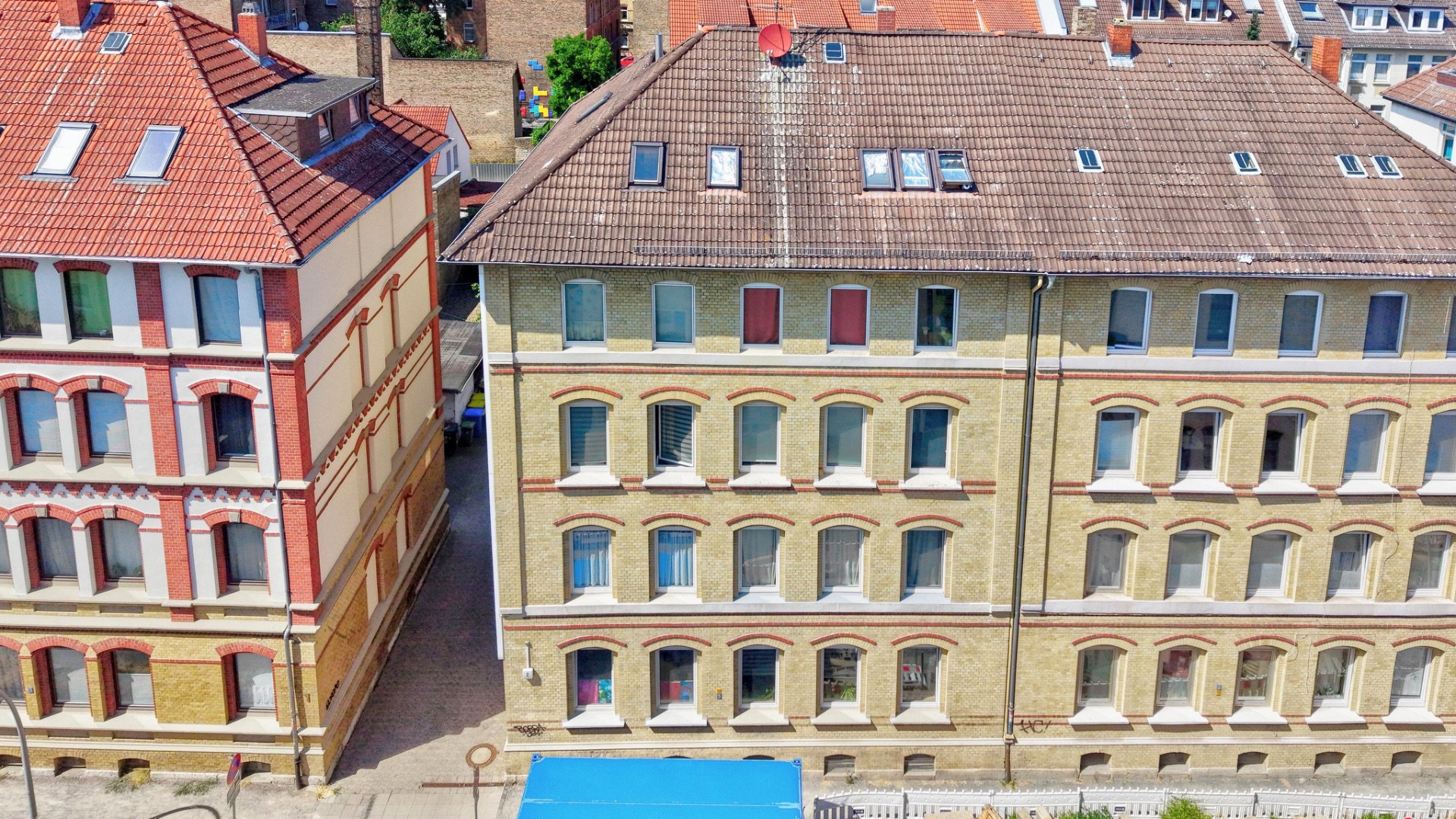 Zwei mehrstöckige Wohngebäude mit vielen Fenstern und Ziegeldächern, von oben fotografiert.