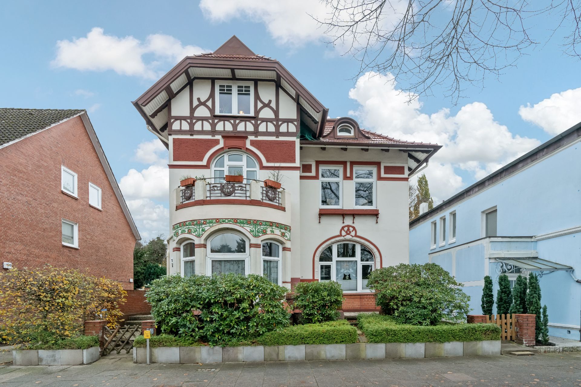 Villenartiges Wohnhaus mit Erker, Balkon und verziertem Giebel, umgeben von Sträuchern.