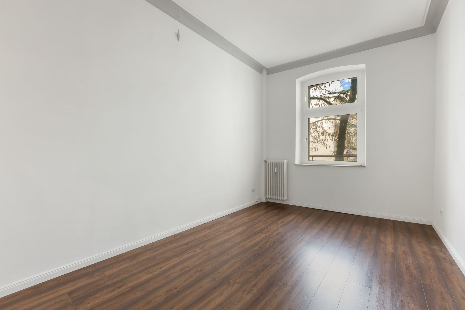 Leerer Raum mit weißer Wand, Holzfußboden, Fenster und Heizkörper.
