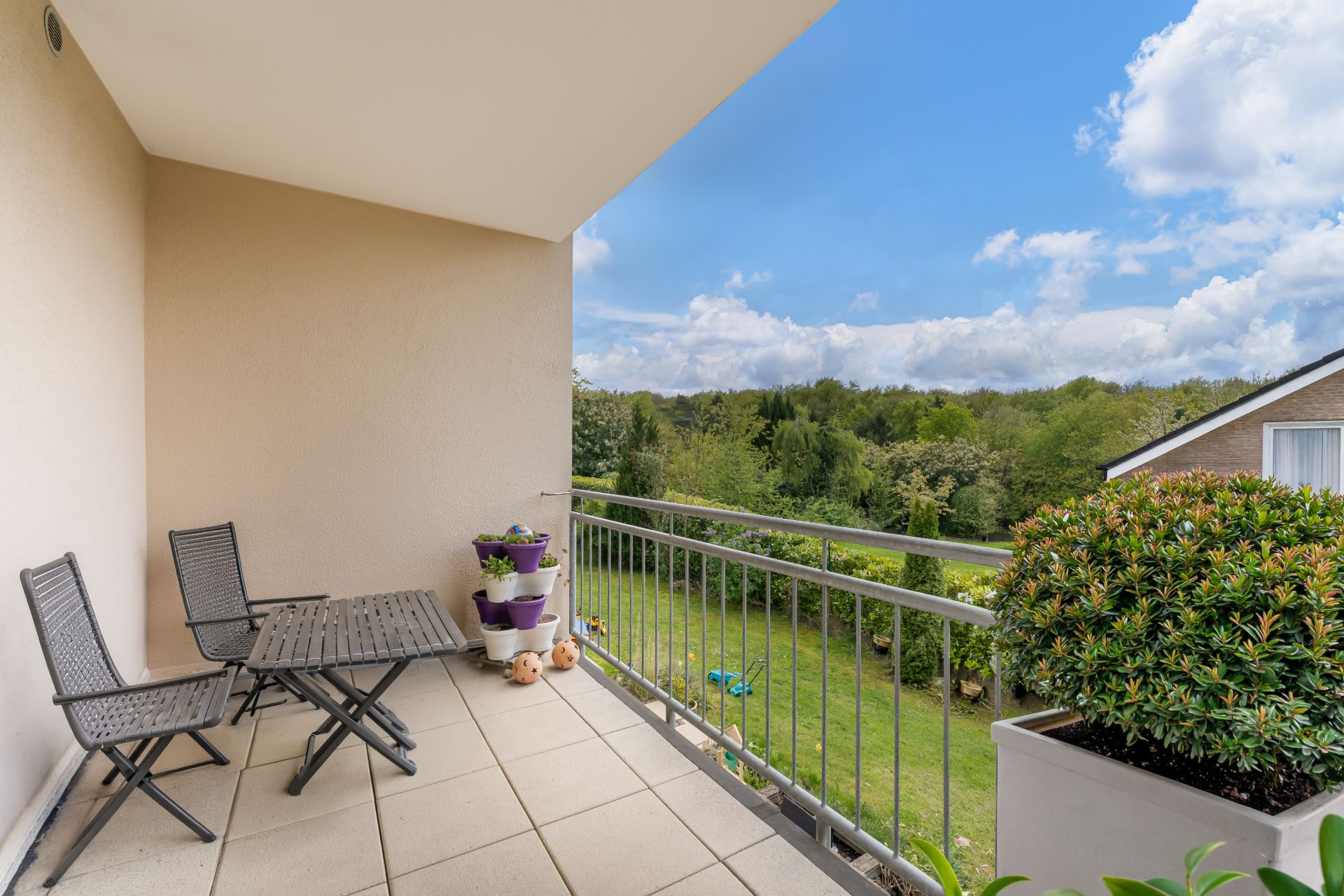 Balkon mit zwei Stühlen, Tisch, Pflanzen und Blick auf einen grünen Garten.