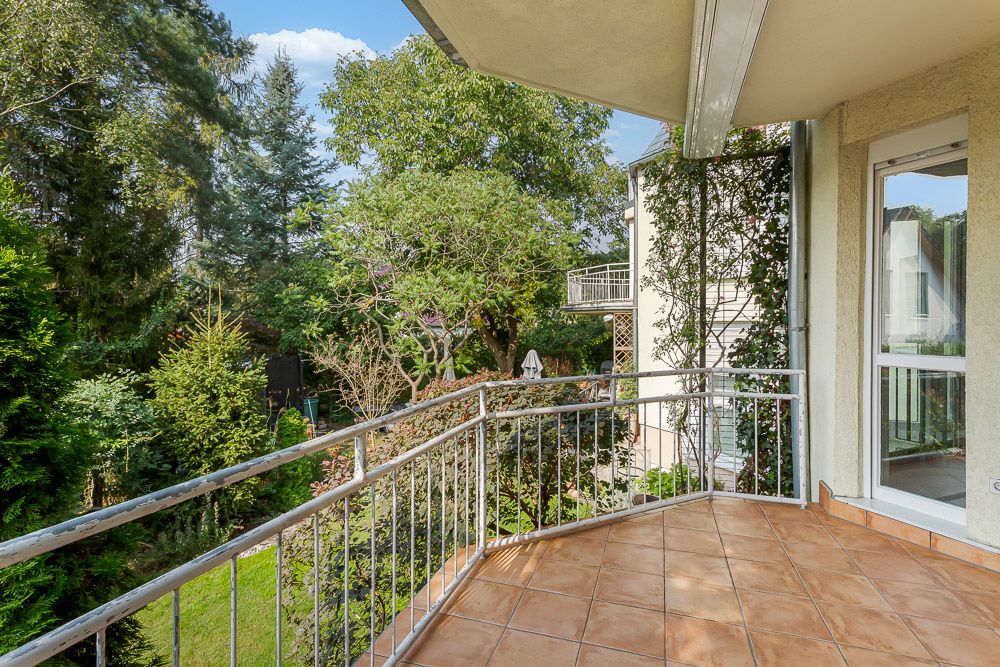Balkon mit braunen Fliesen, Metallgeländer und Blick auf einen grünen Garten.
