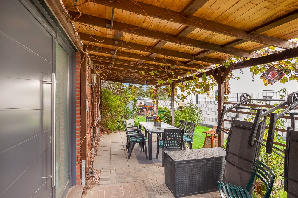 Überdachte Terrasse mit Esstisch, Stühlen und Gartenmöbeln, umgeben von Grünpflanzen.