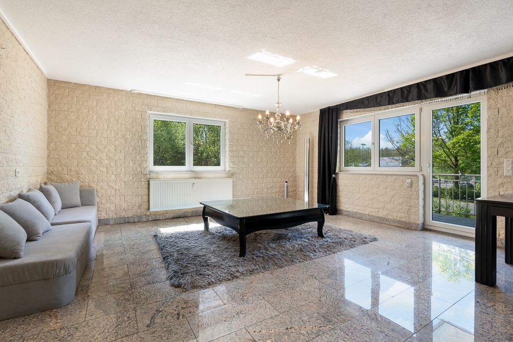Helles Wohnzimmer mit grauem Sofa, schwarzem Tisch und großem Teppich auf Fliesenboden.