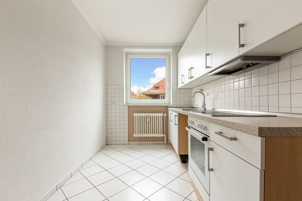 Helle Küche mit weißen Fliesen, weißen Schränken und Fenster mit Blick nach draußen.