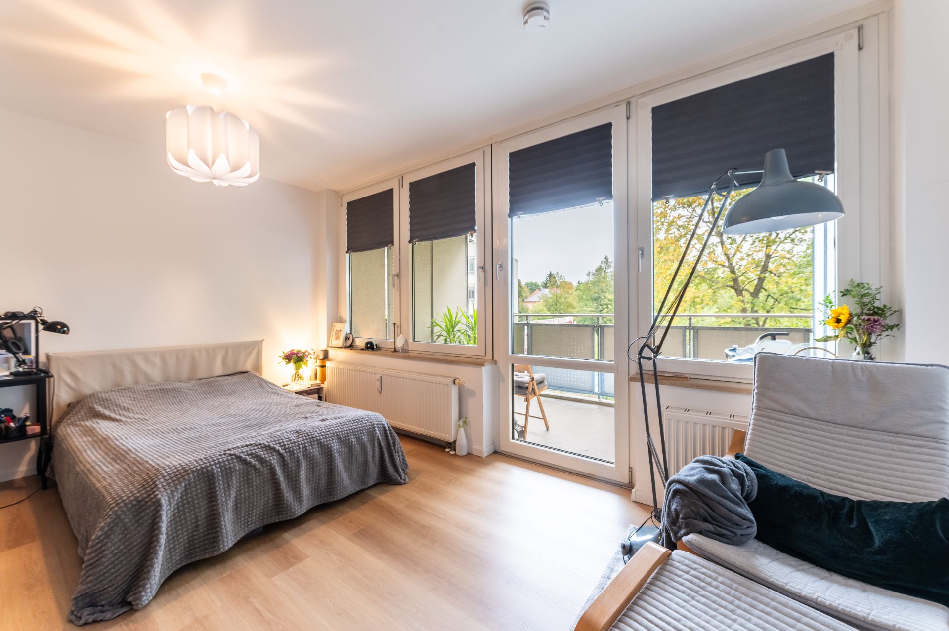 Helles Schlafzimmer mit Doppelbett, Sessel, großen Fenstern und Zugang zu einem Balkon.