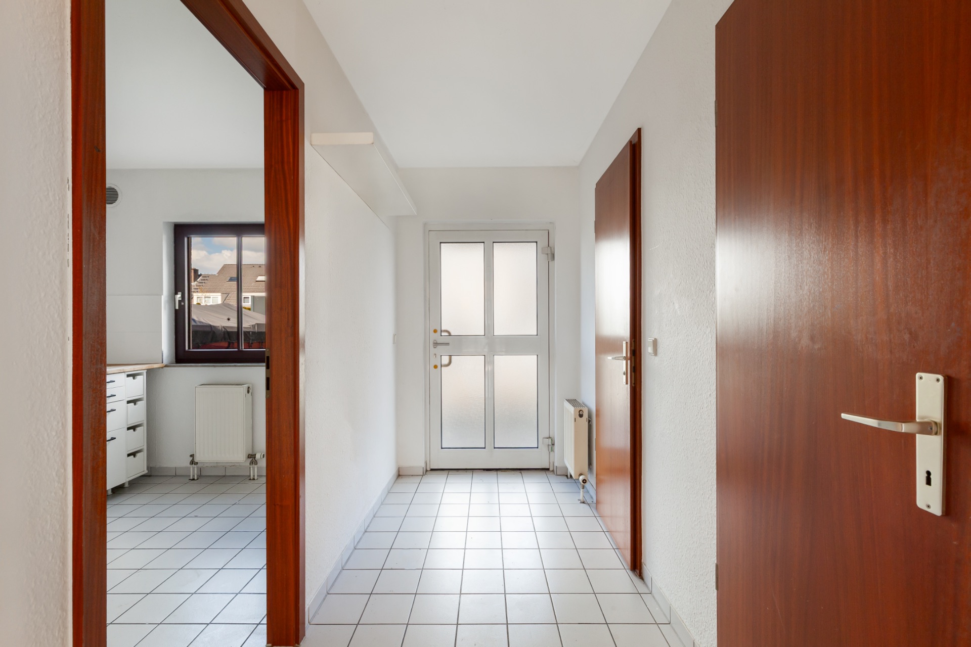 Heller Flur mit Fliesenboden, Holztüren und Zugang zur Küche mit Fenster.