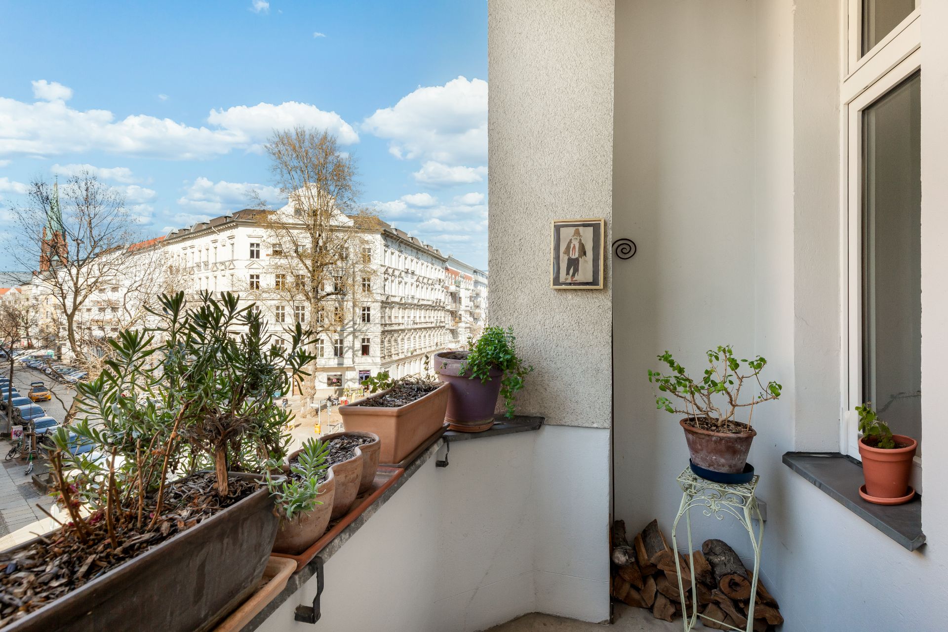 Balkon mit mehreren Pflanzen in Töpfen und Blick auf eine Wohnstraße mit alten Gebäuden.