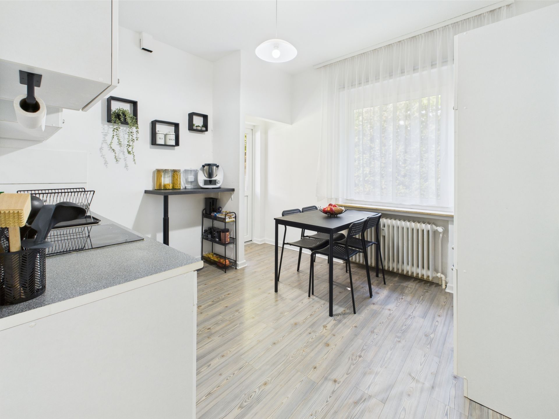 Helle Küche mit Esstisch, vier Stühlen und großem Fenster mit Vorhängen.