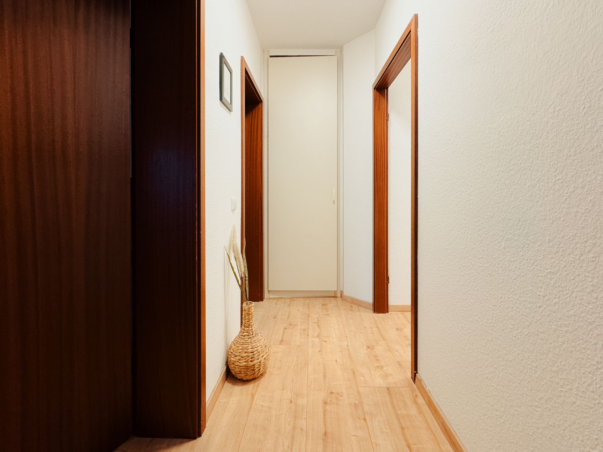 Heller Flur mit Holzboden, Türen und einem Korb mit Zweigen an der Wand.