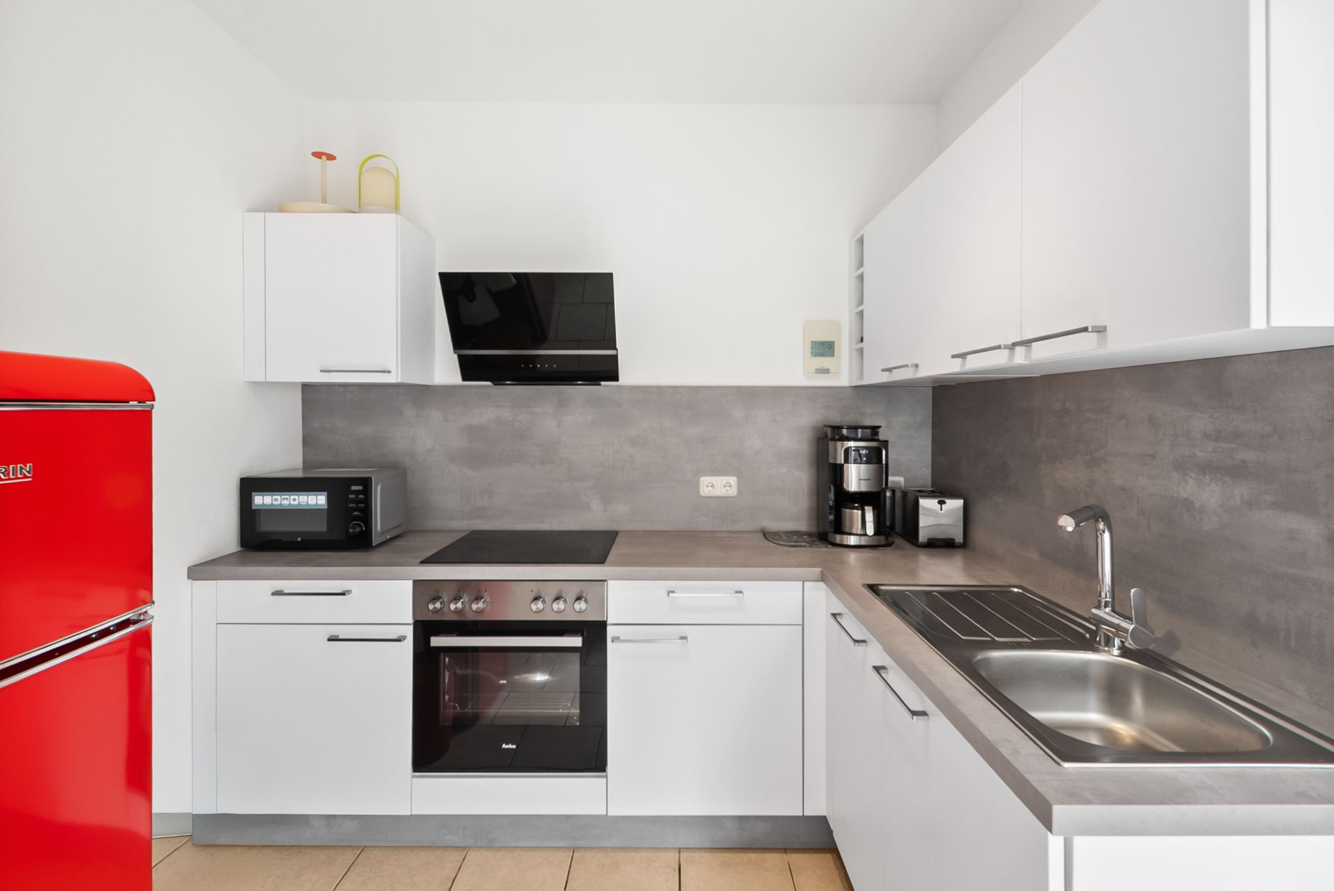 Moderne weiße Einbauküche mit rotem Kühlschrank, Herd, Spüle und Kaffeemaschine.