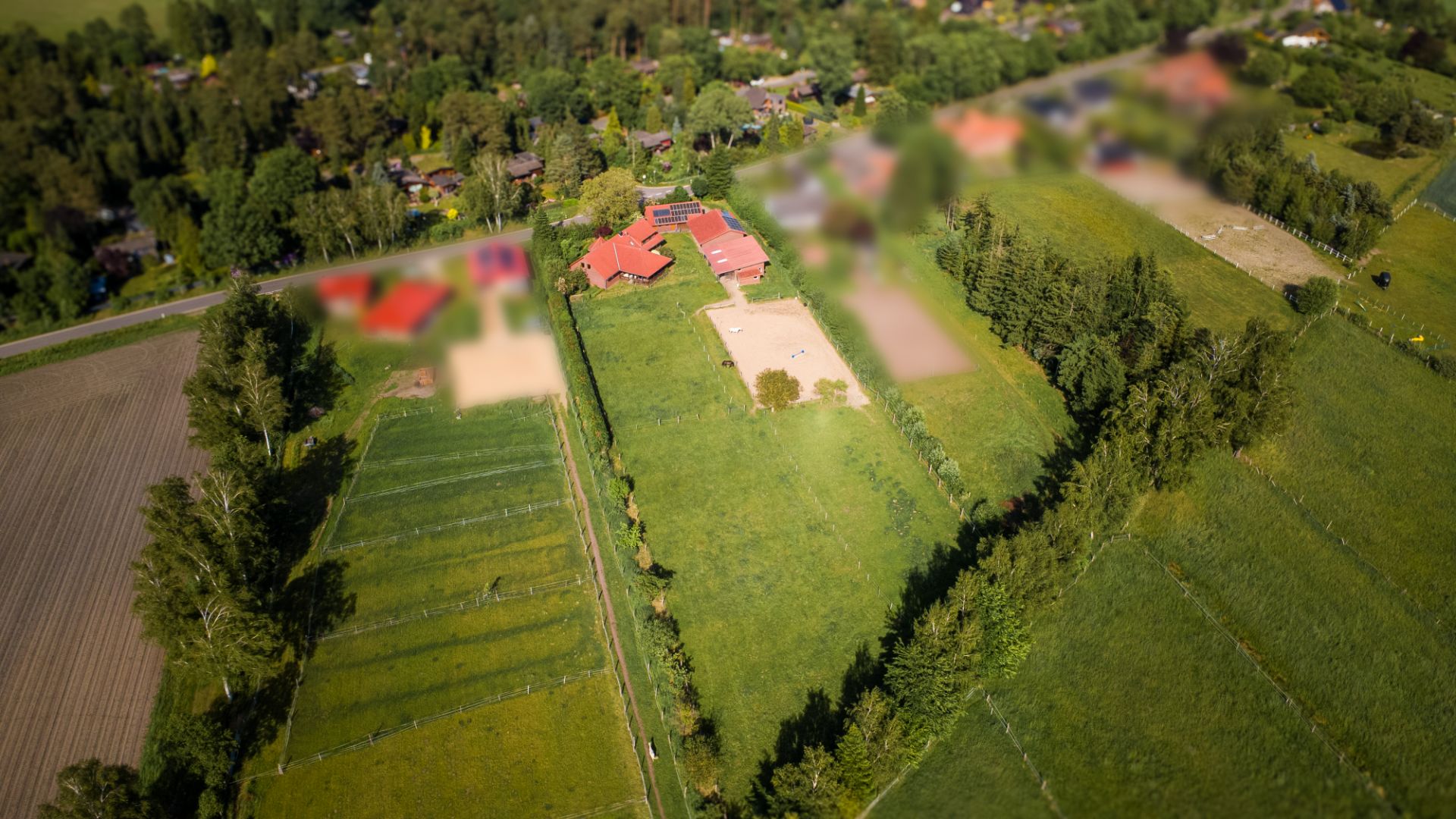 Luftaufnahme eines Wohnhauses mit roten Dächern, umgeben von großen grünen Wiesen und Bäumen.