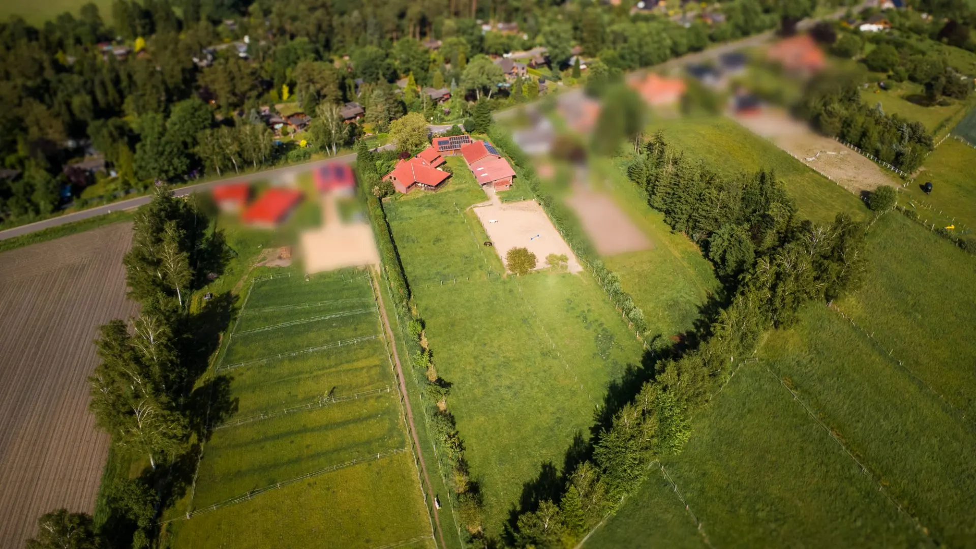 Luftaufnahme eines Wohnhauses mit roten Dächern, umgeben von großen grünen Wiesen und Bäumen.