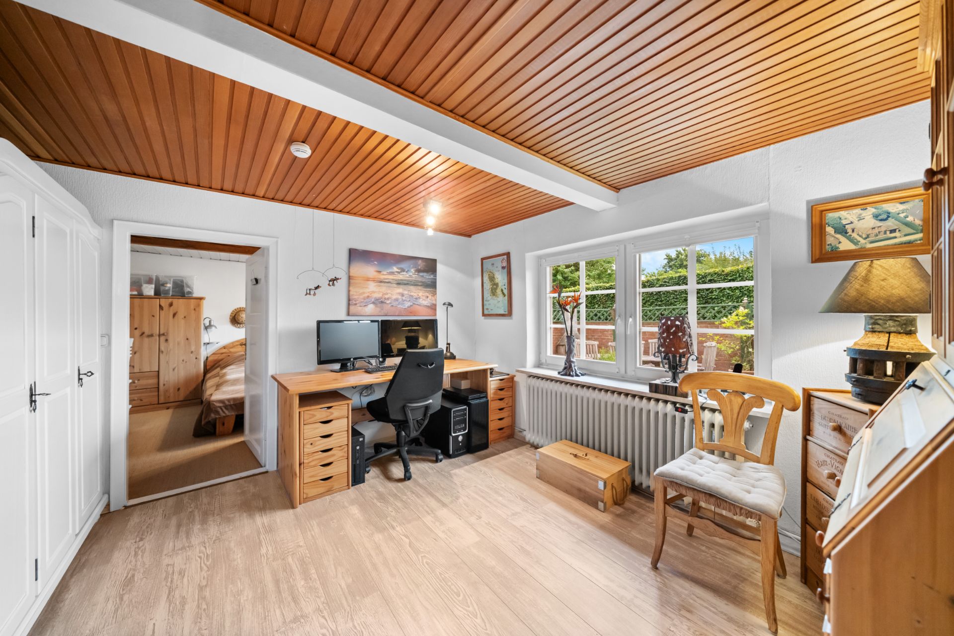 Helles Arbeitszimmer mit Holzdecke, großem Schreibtisch, Stuhl und Fenstern zum Garten.