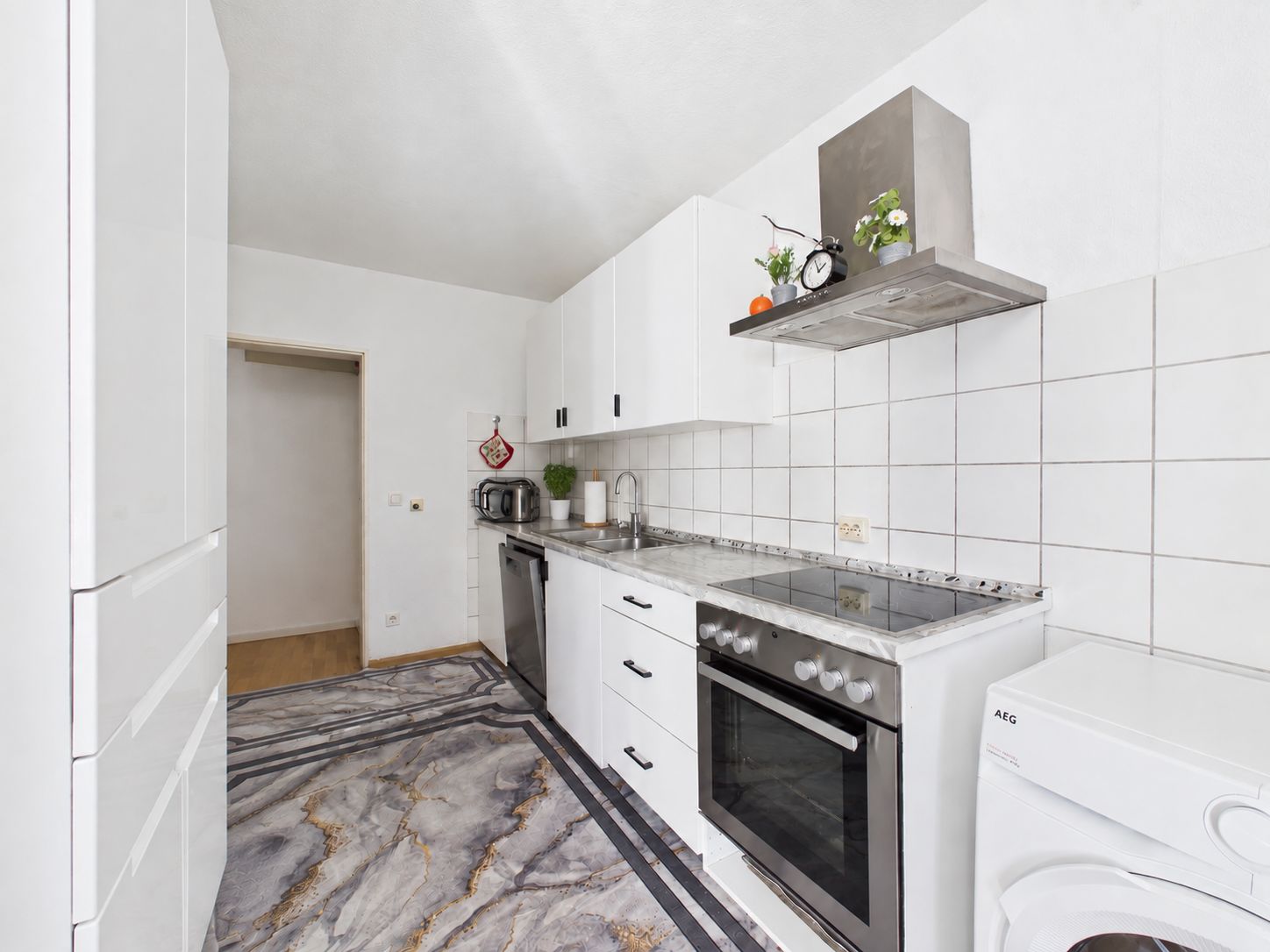 Moderne weiße Küche mit Herd, Spüle, Waschmaschine und Schränken.