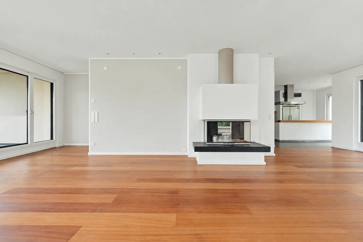Helles Wohnzimmer mit Kamin, großen Fenstern und Holzfußboden.