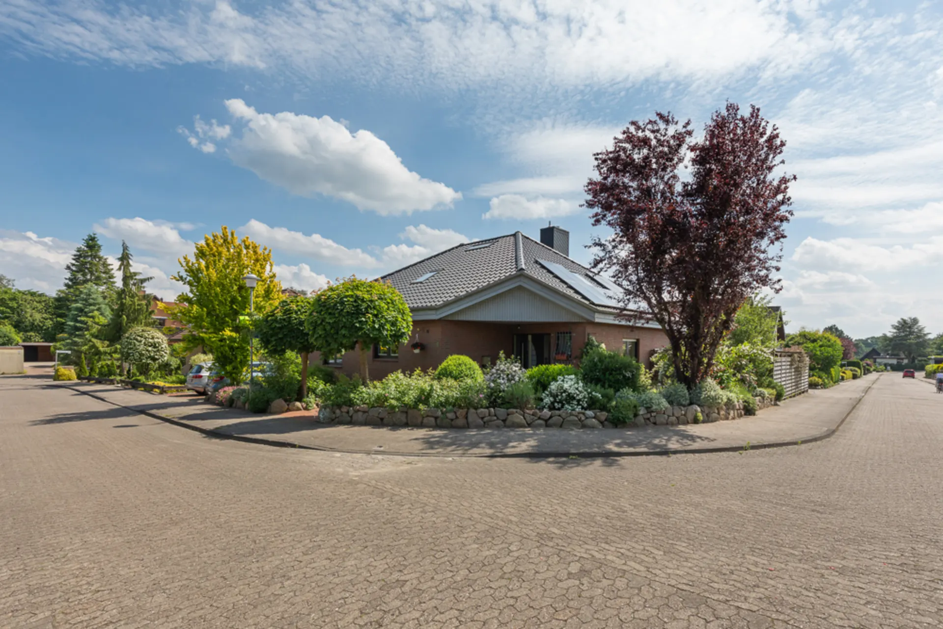 Einfamilienhaus an einer ruhigen Straße, umgeben von gepflegtem Garten und Bäumen.