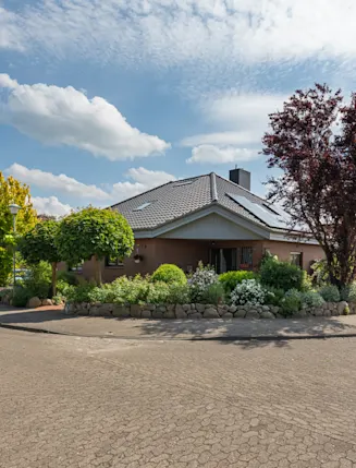 Einfamilienhaus an einer ruhigen Straße, umgeben von gepflegtem Garten und Bäumen.
