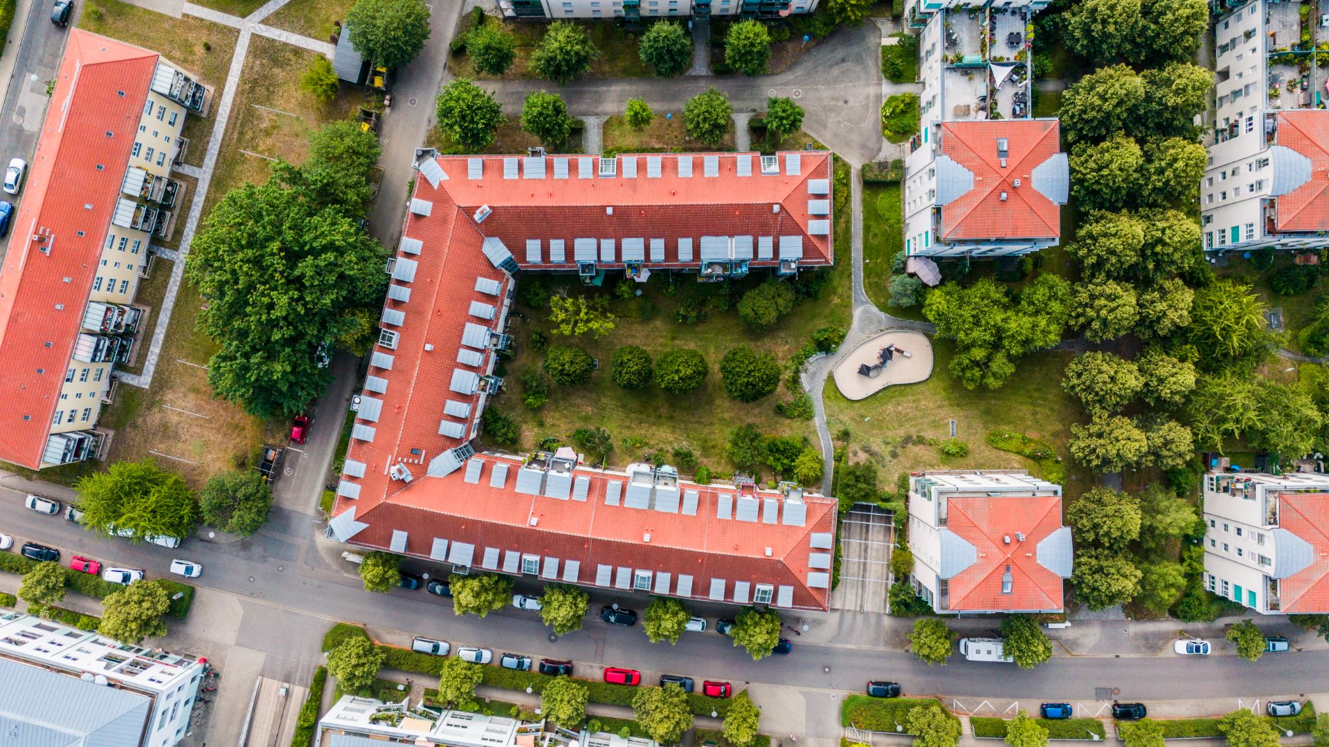 Luftaufnahme eines Wohngebäudekomplexes mit rotem Dach und grünem Innenhof.