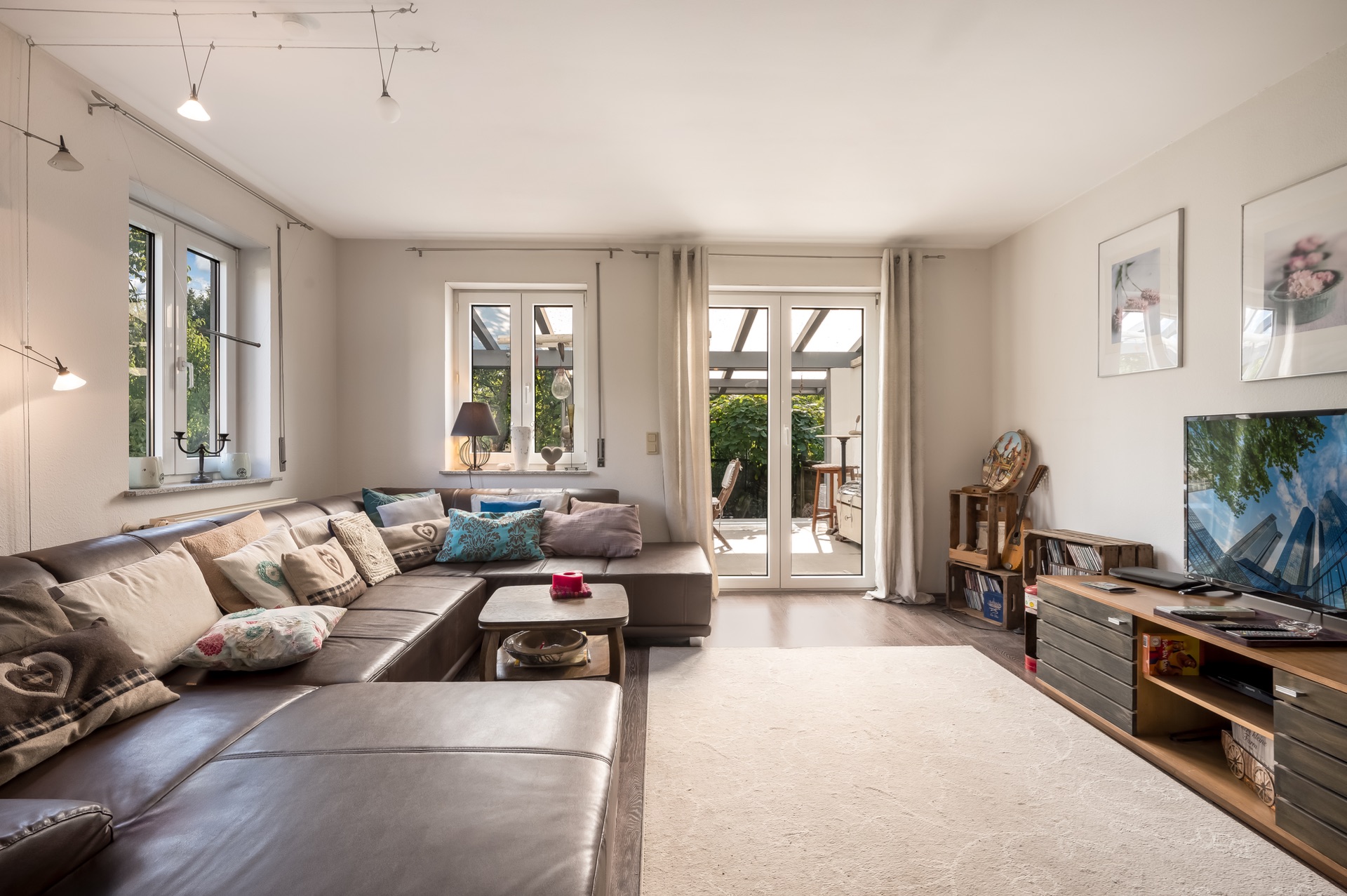 Helles Wohnzimmer mit großer Eckcouch, Fernseher, Couchtisch und Zugang zur Terrasse.