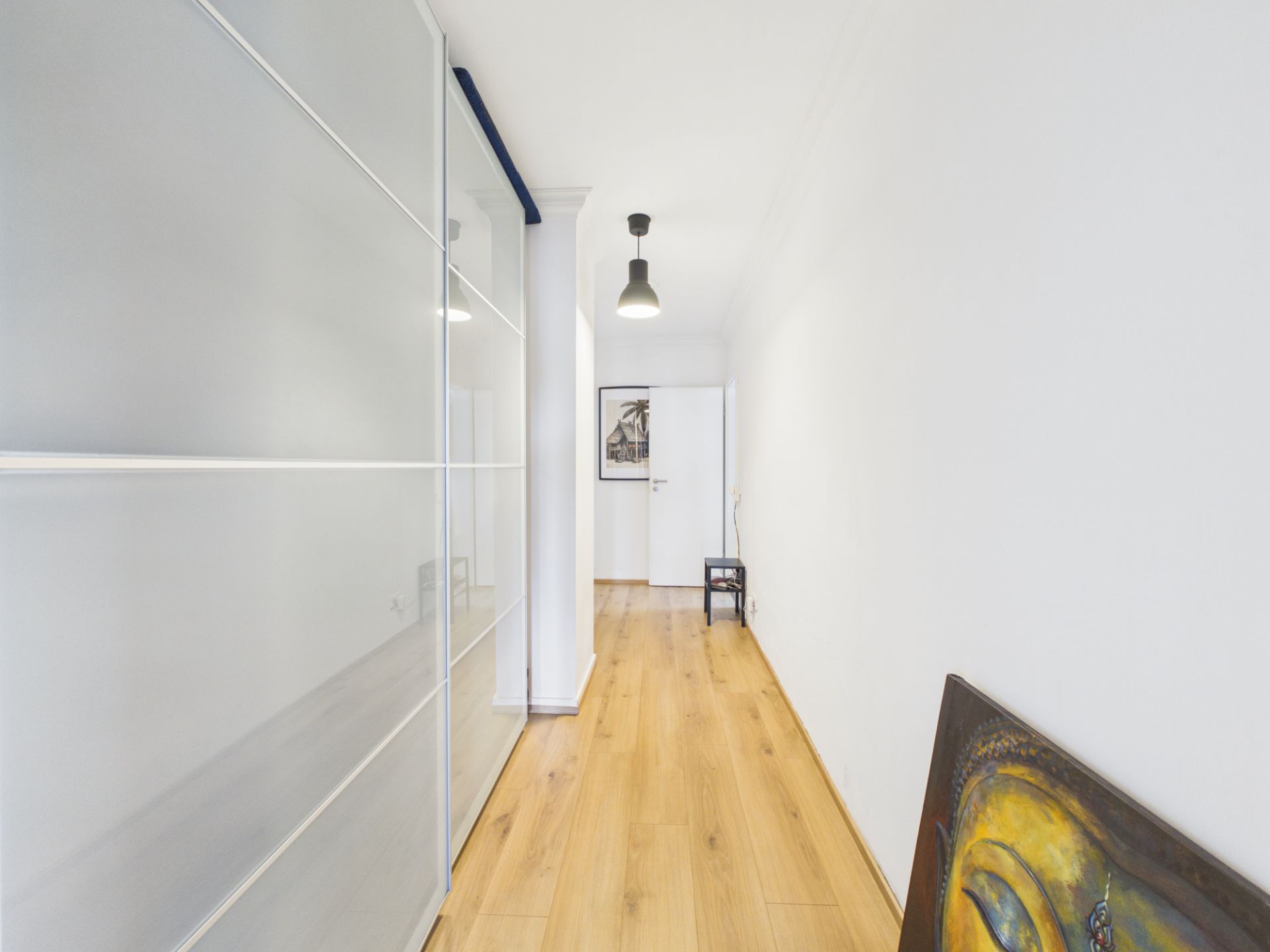 Heller Flur mit Holzfußboden, Glastüren links und einem Bild an der rechten Wand.
