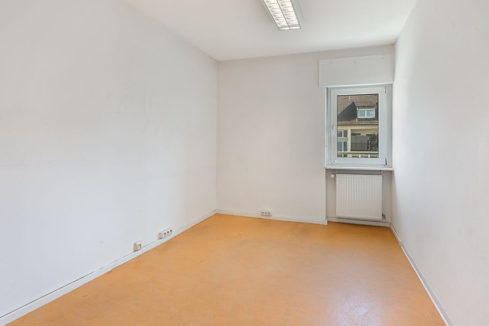 Leeres Zimmer mit orangem Boden, weißer Wand, Fenster und Heizkörper unter dem Fenster.