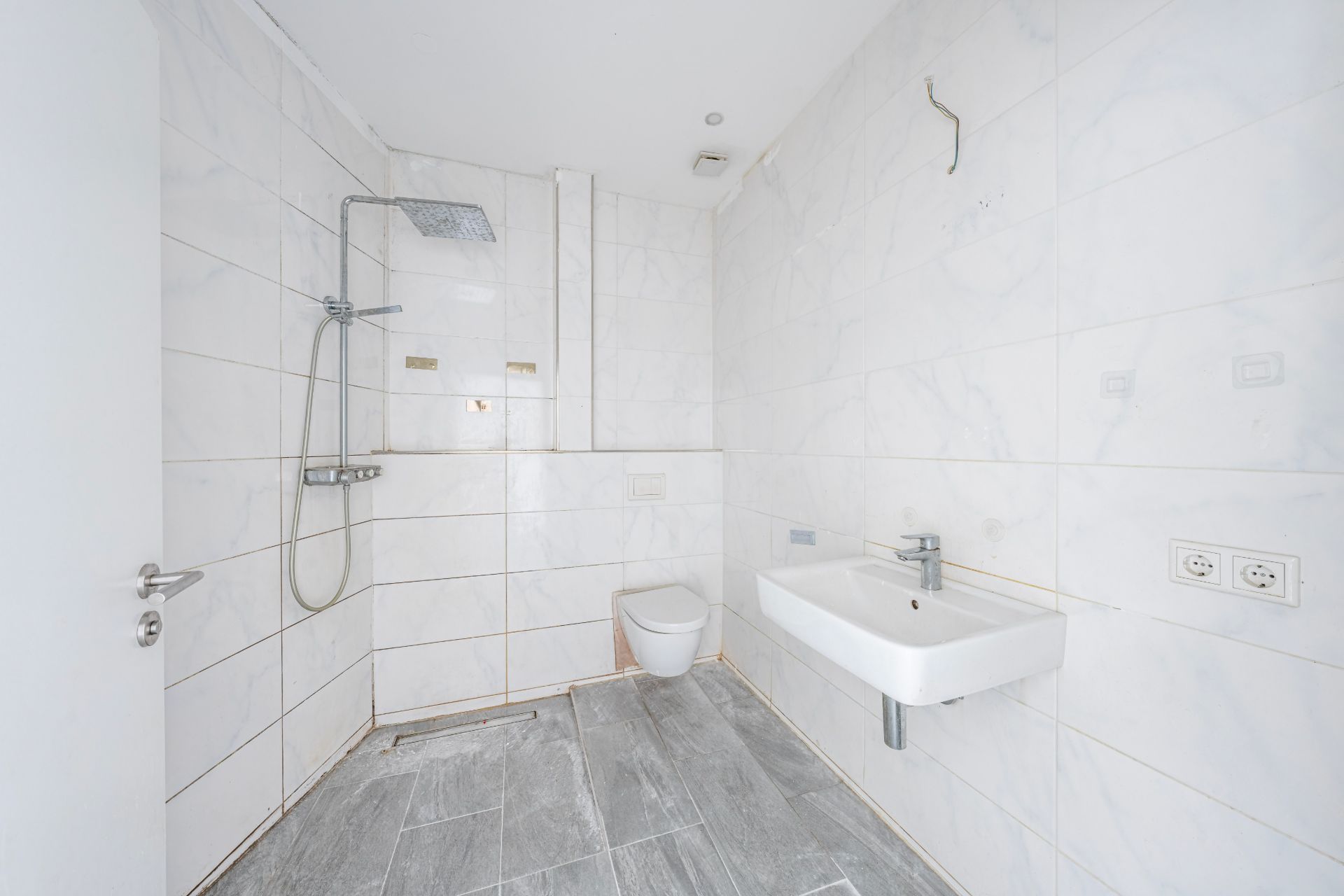 Modernes, weiß gefliestes Badezimmer mit Dusche, Wand-WC und Waschbecken.
