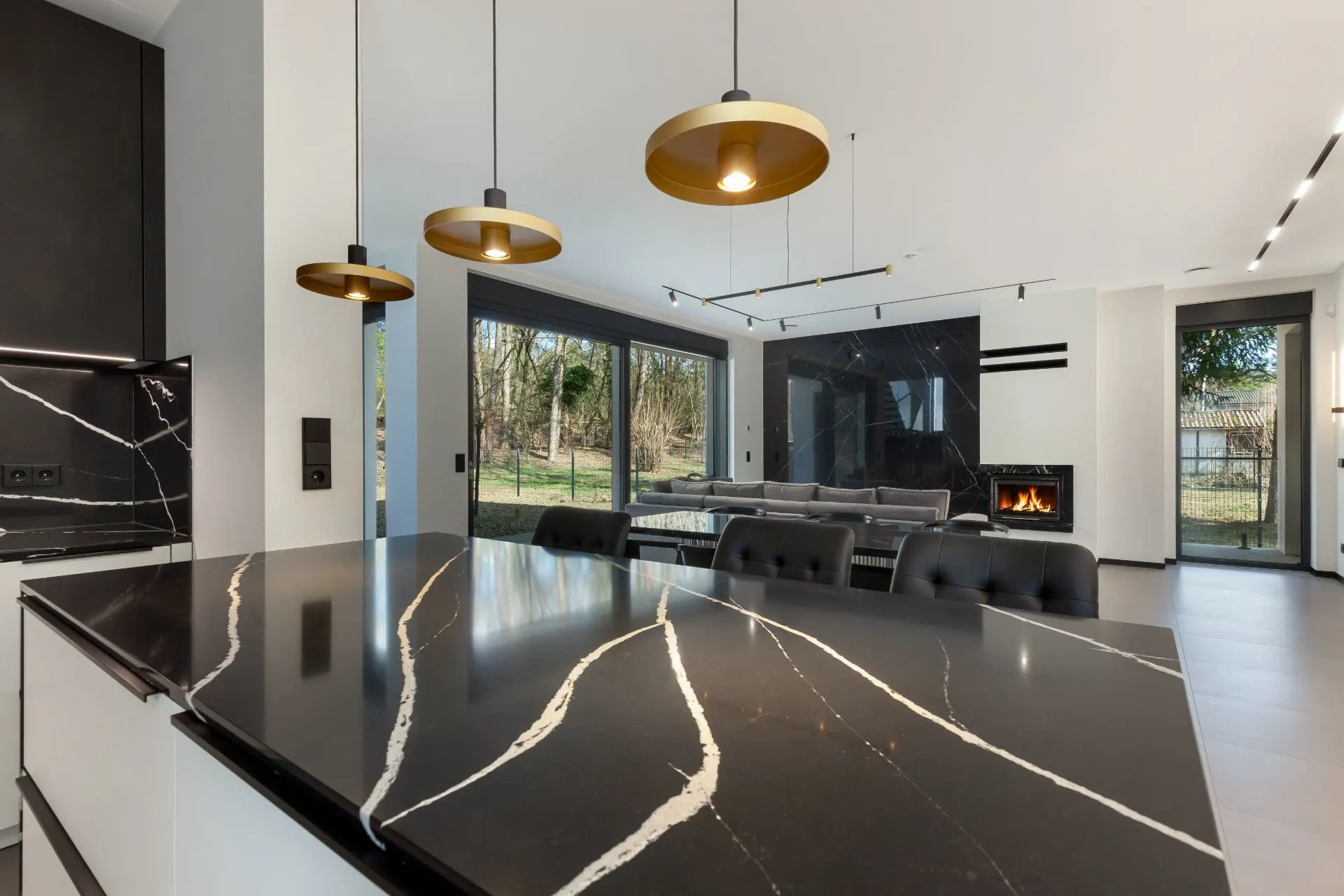 Moderne offene Küche mit schwarzer Marmortheke, großen Fenstern und Blick ins Wohnzimmer mit Kamin.