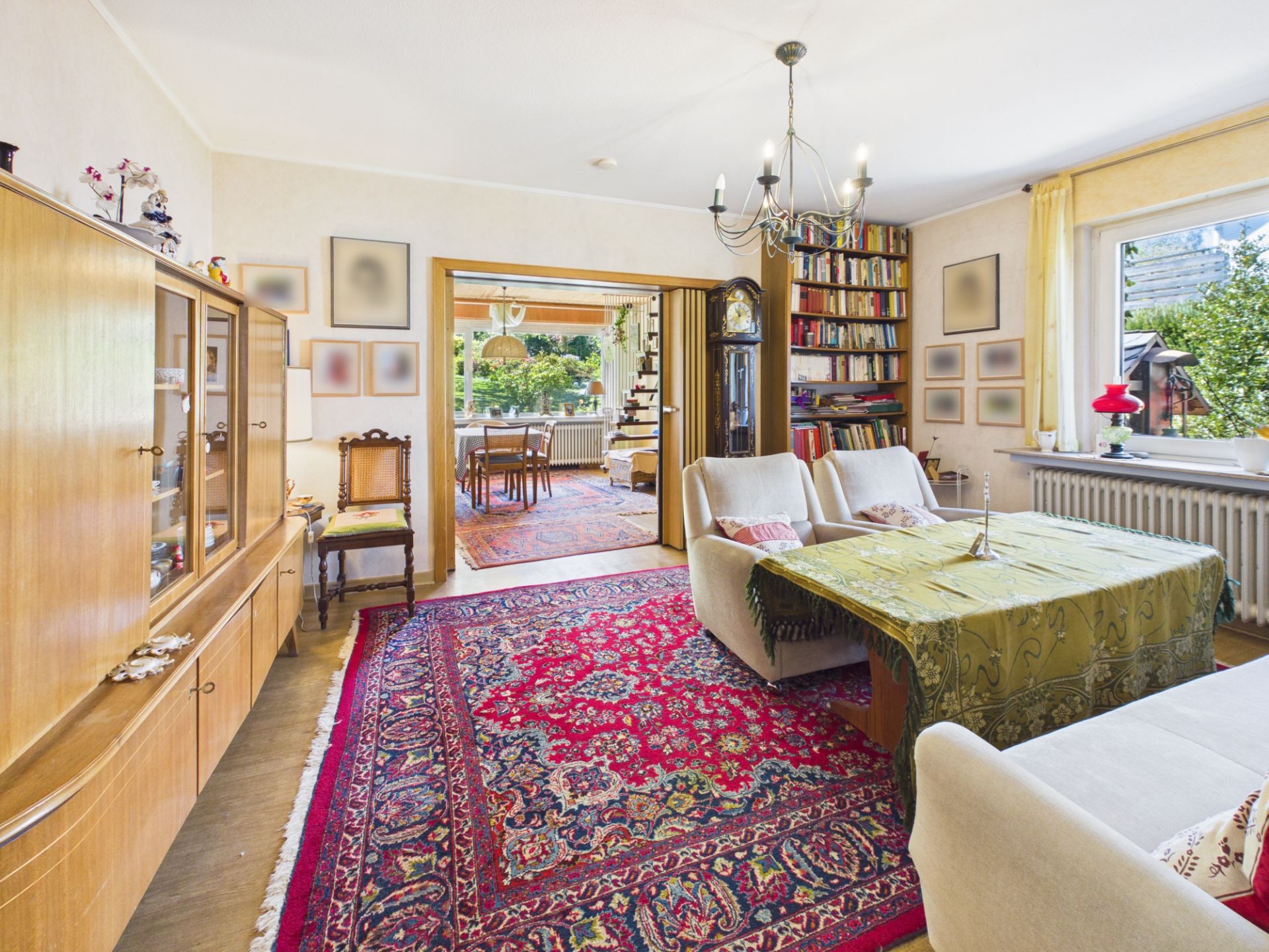 Wohnzimmer mit Teppich, Sofas, großem Fenster, Regal und Durchgang zu Esszimmer mit Gartenblick.