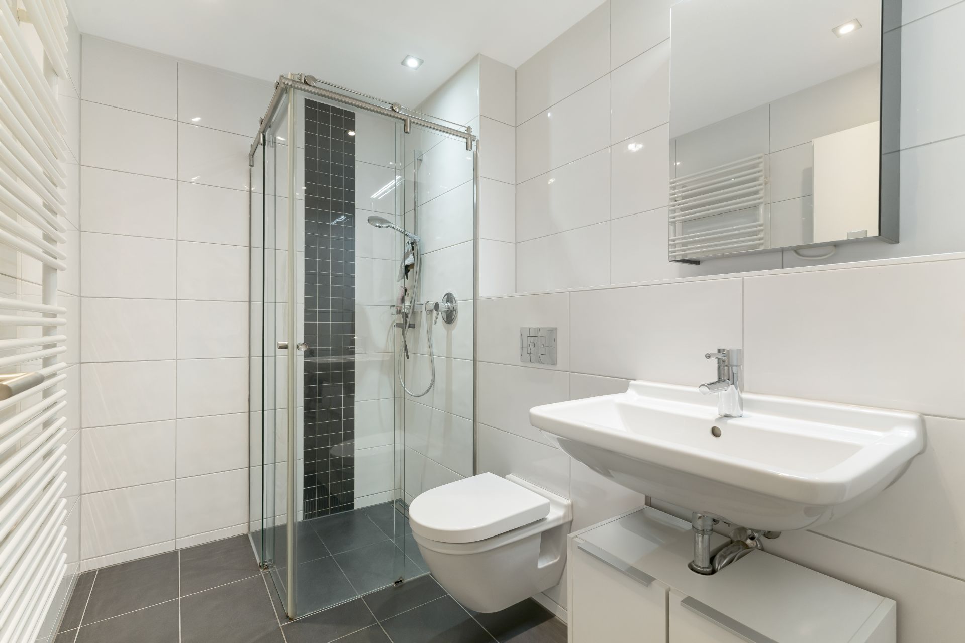Modernes Bad mit Glasdusche, Waschbecken und wandhängendem WC, weiße Fliesen.