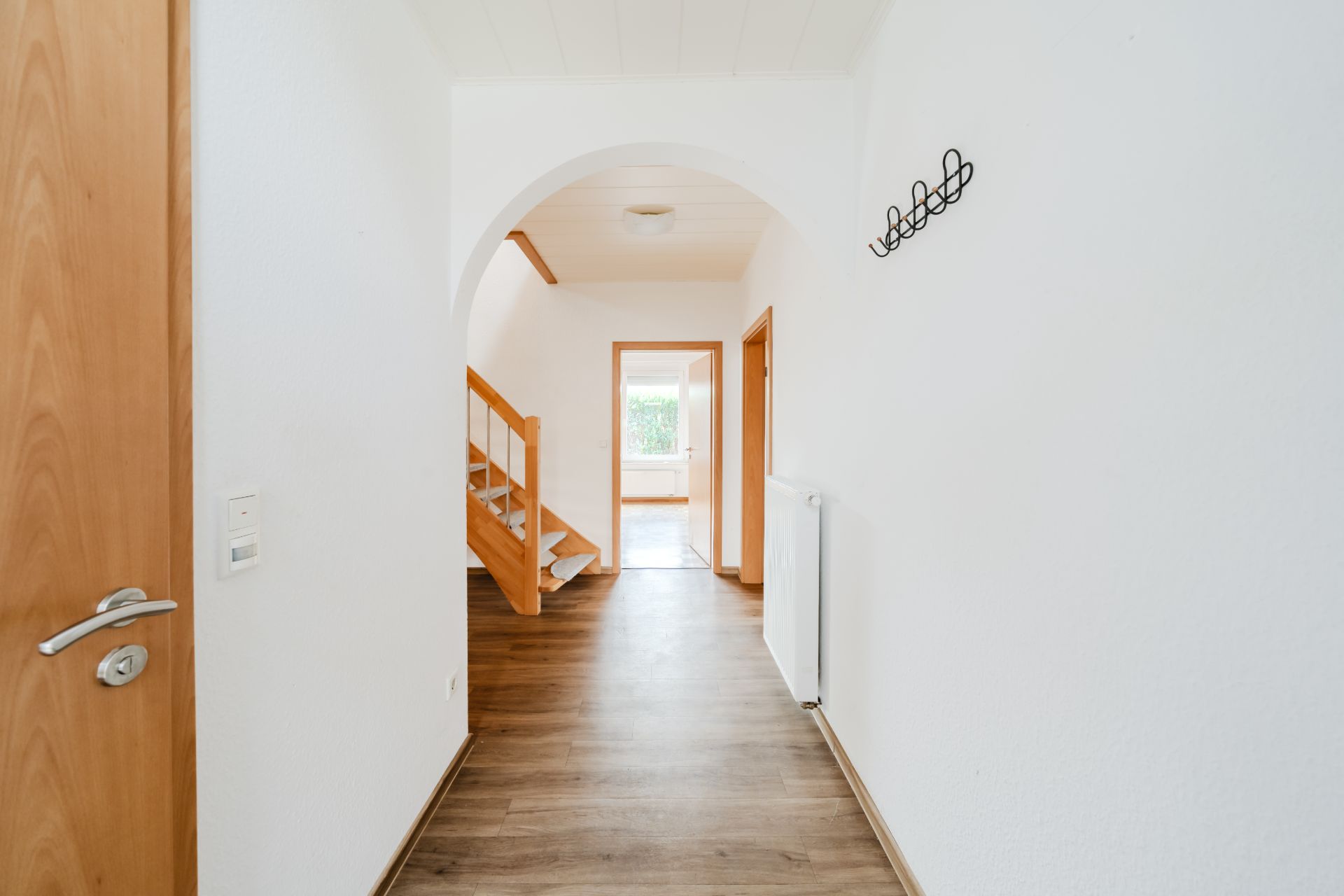Heller Flur mit Holztür, Holztreppe, Bogen und Garderobenhaken an der Wand.