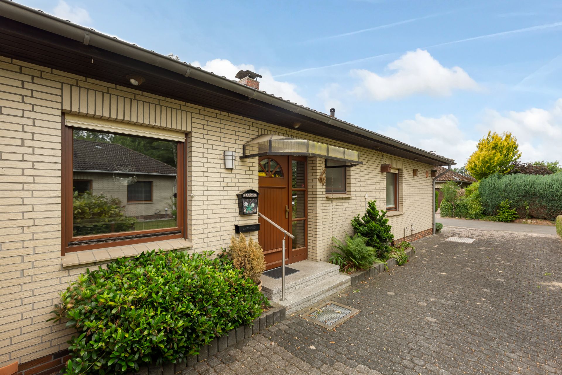 Vorderansicht eines einstöckigen Hauses mit Klinkerfassade, Haustür und großem Fenster.