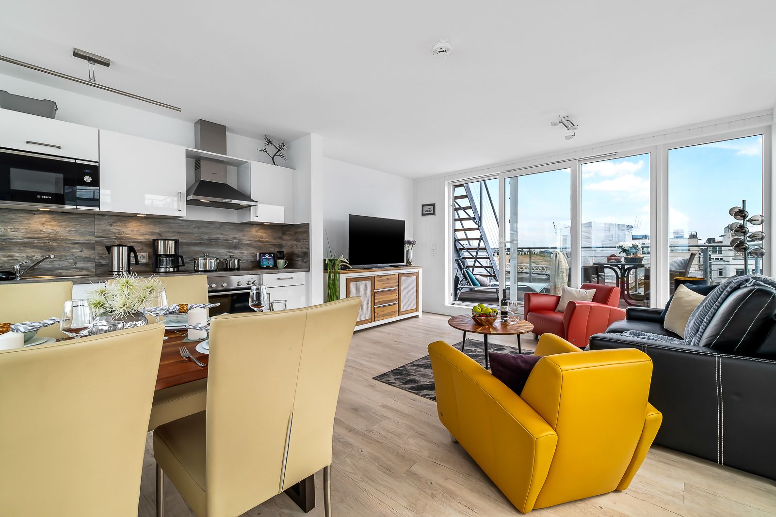Helle Wohnküche mit Esstisch, Sitzecke, großer Fensterfront und Zugang zum Balkon.