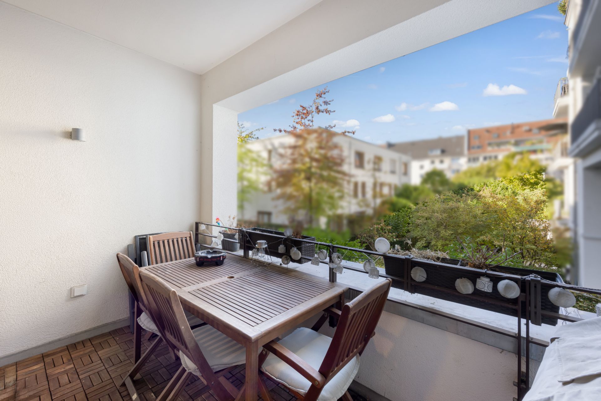 Überdachter Balkon mit Holztisch und vier Stühlen, Blick auf Garten und Nachbarhäuser.