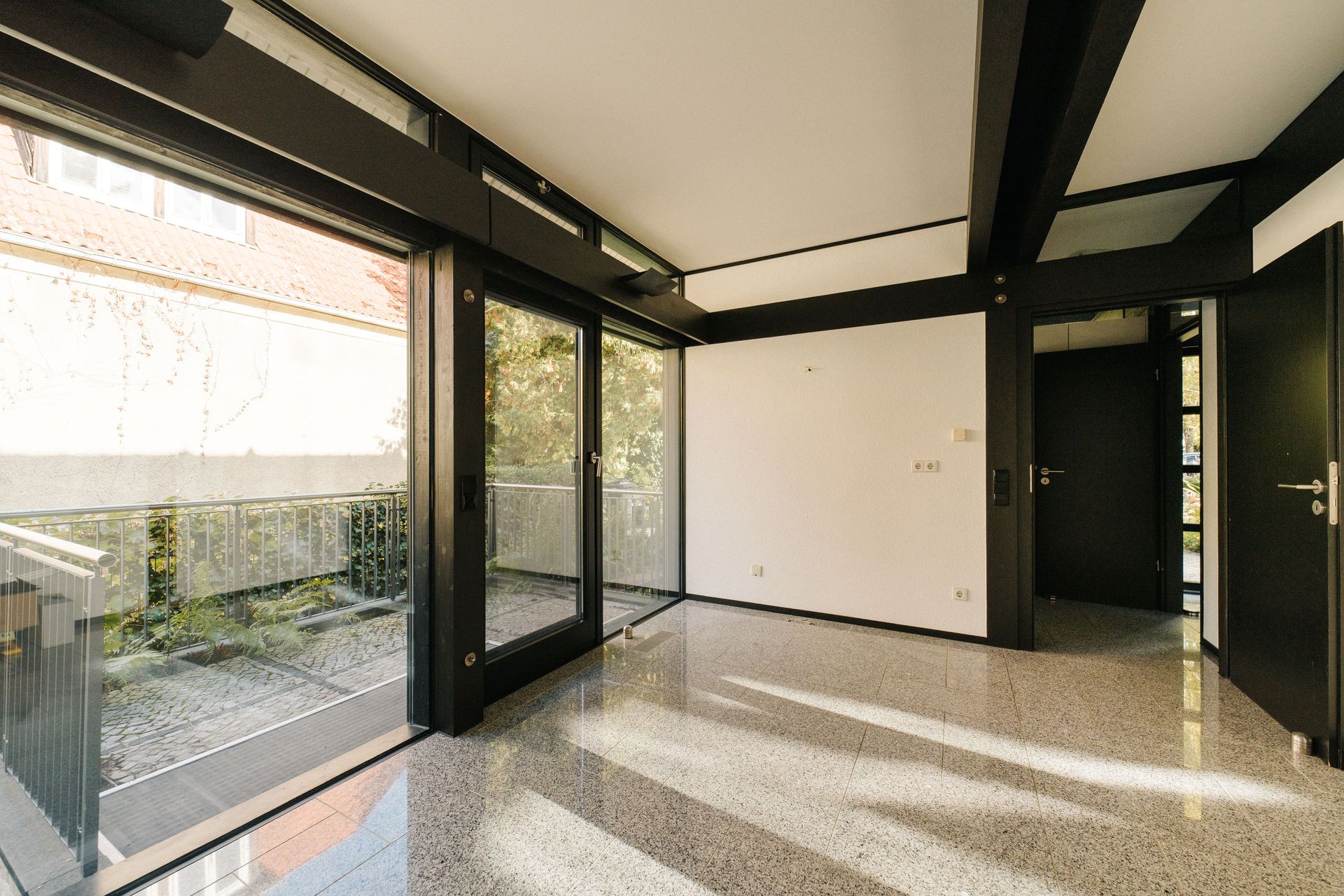 Heller Raum mit großen Fenstern, Glastüren und Zugang zur Terrasse.