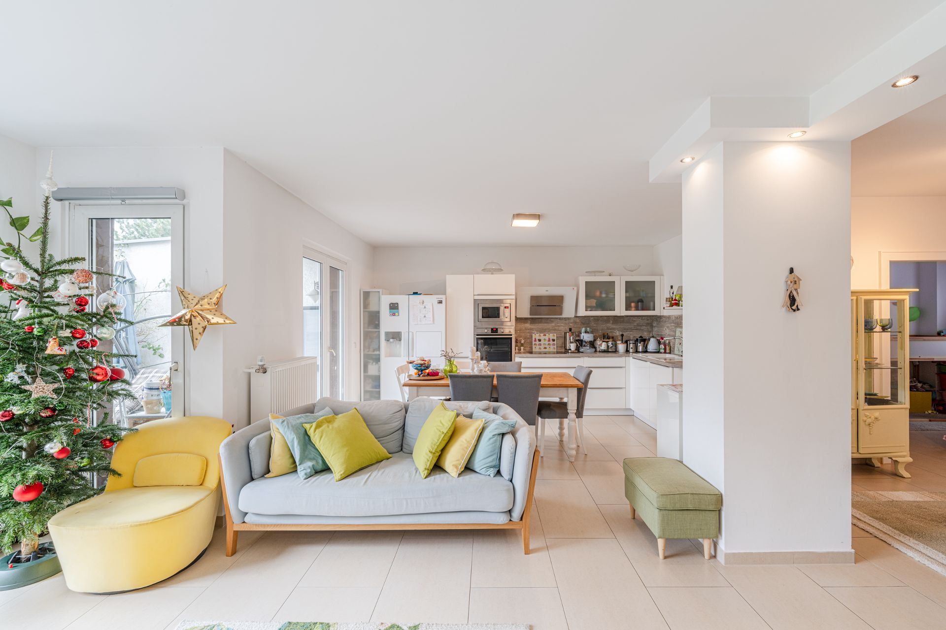 Helles Wohnzimmer mit Sofa, Sessel, Weihnachtsbaum und offener Küche im Hintergrund.