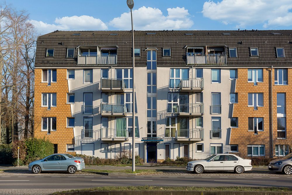 Mehrstöckiges Wohnhaus mit Balkonen, Autos parken davor auf der Straße.
