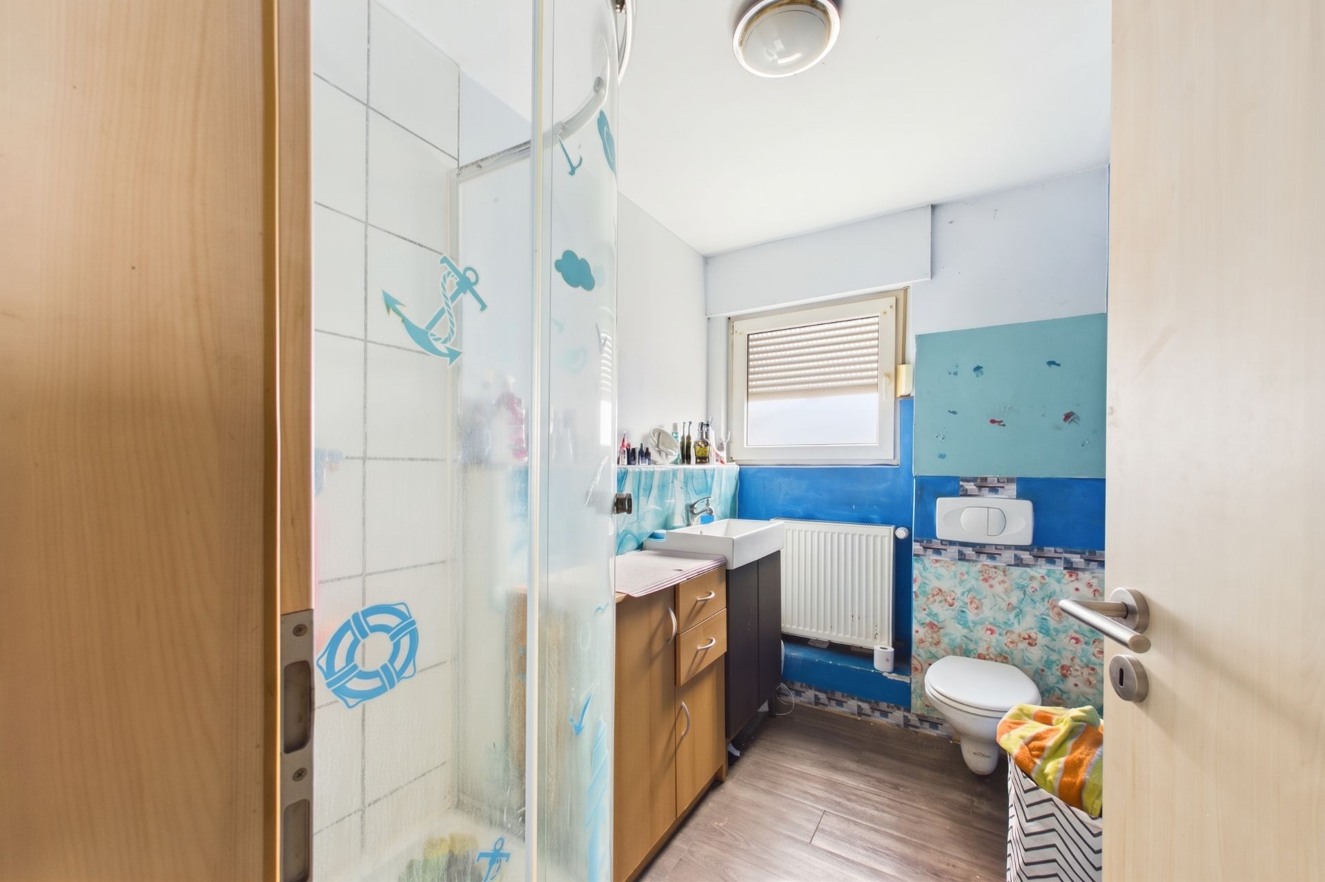 Kleines Badezimmer mit Dusche, WC, Waschbecken und bunten Wandmotiven.