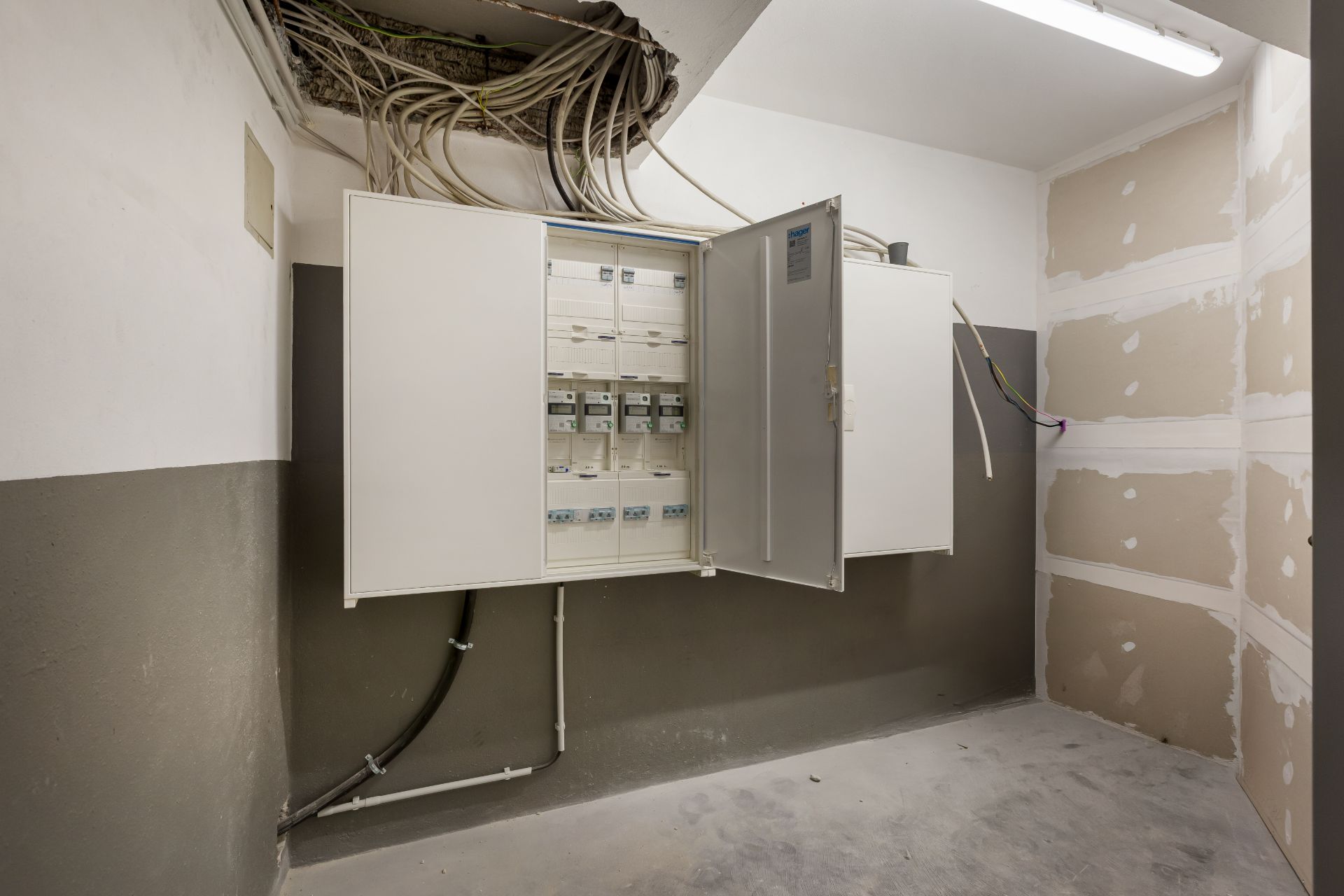 Elektroraum mit offenem Sicherungskasten und sichtbaren Kabeln an der Decke.
