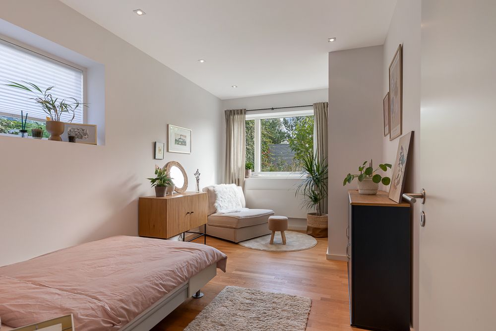 Helles Schlafzimmer mit Einzelbett, Sessel, Pflanzen und großem Fenster mit Blick ins Grüne.